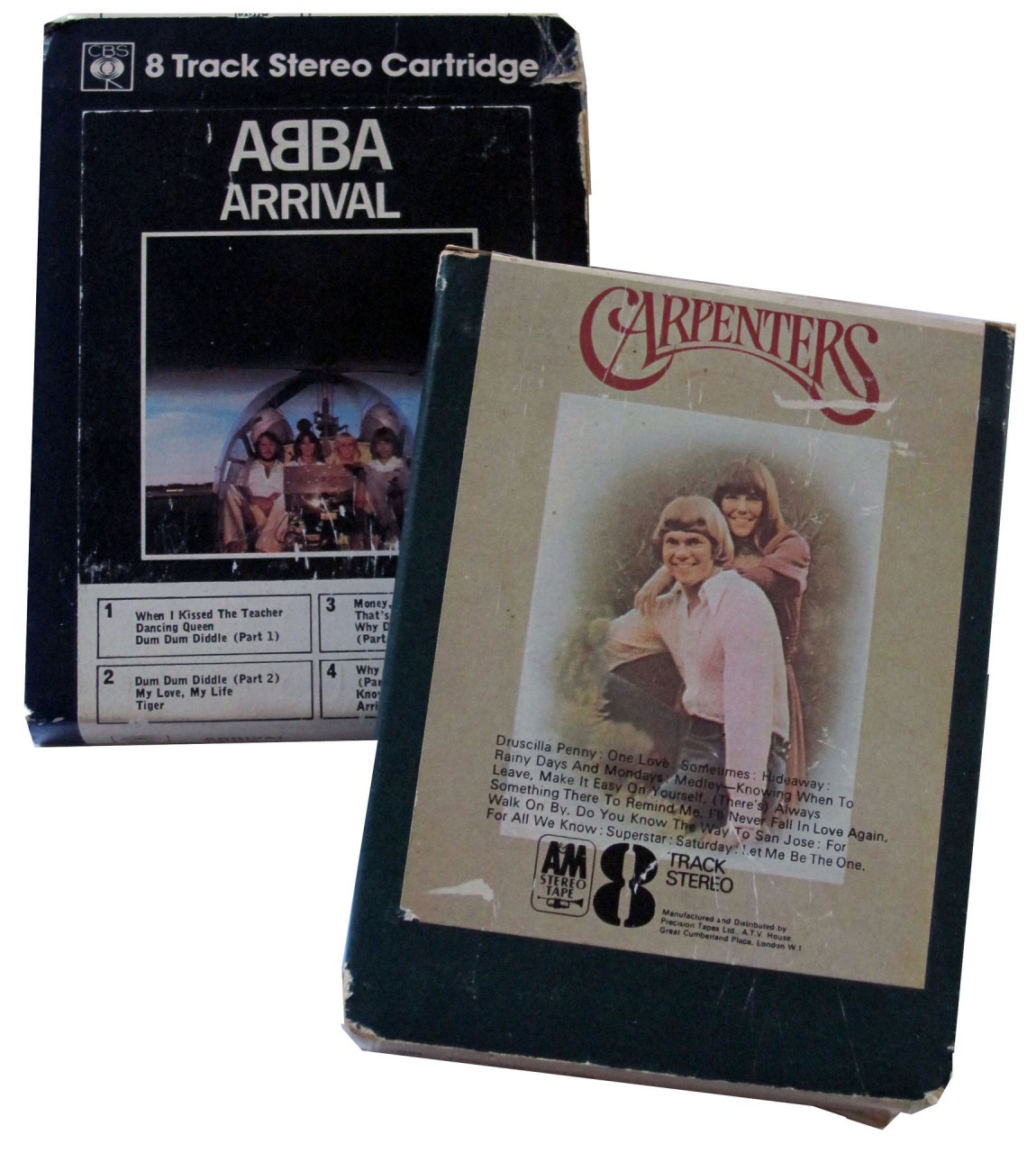 Two 8-track stereo cartridges, one featuring ABBA's "Arrival" album and the other by the Carpenters. The ABBA cartridge has a black cover with an image of the band, while the Carpenters' cartridge shows a picture of Karen and Richard Carpenter embracing, with a list of songs on the back.